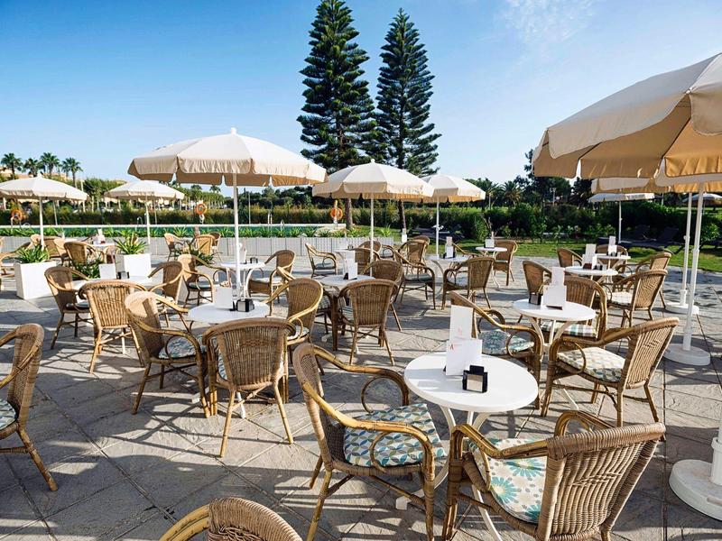 Leerer Außenbereich eines Cafés mit runden Tischen, Stühlen und hellen Sonnenschirmen bei Sonnenschein.