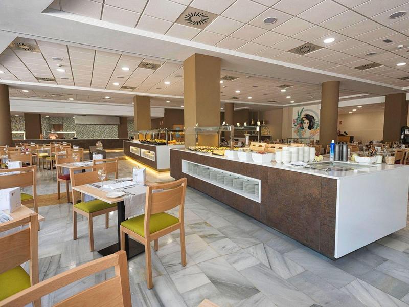 Großer heller Speisesaal mit Holzstühlen, Tischen und Buffetinsel mit Getränken und Snacks.