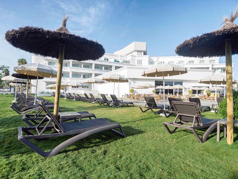 Hell eingerichtetes Hotelzimmer mit Doppelbett, Sofa, Holzschreibtisch und moderner Beleuchtung.