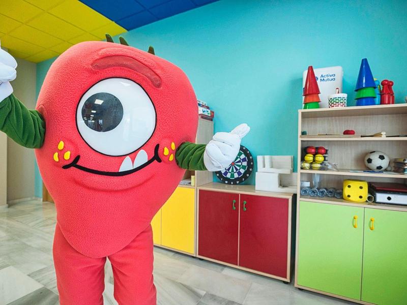 Roter einäugiger Monsterkostüm mit gelben Punkten, gelbem Zahn und Daumen hoch im bunten Kinderzimmer.