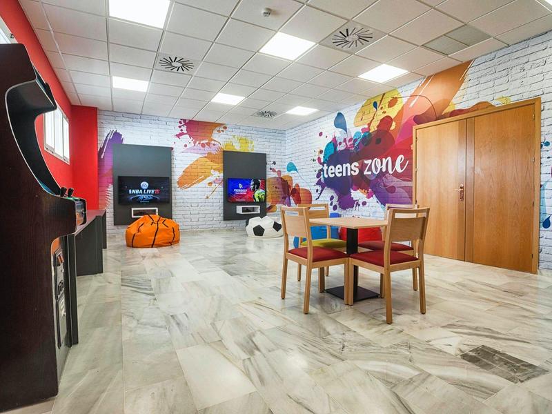 Moderner Raum mit weißen Wänden, bunten Wandbildern, Sitzsäcken und einem Tisch mit Stühlen.