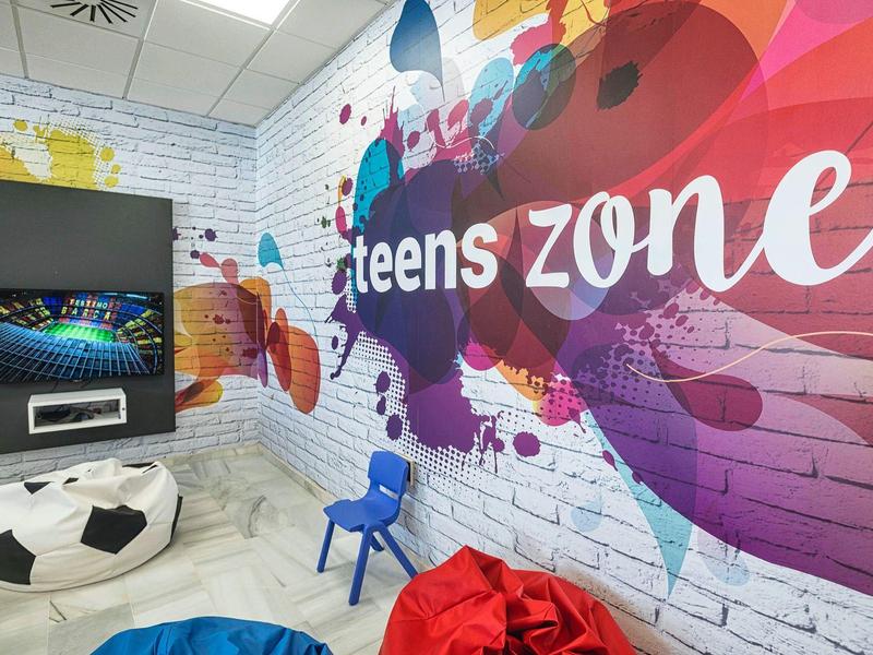 Bunte Teenagerzone mit Sitzsäcken, Fußballhocker, blauem Stuhl und TV an weißer Backsteinwand.