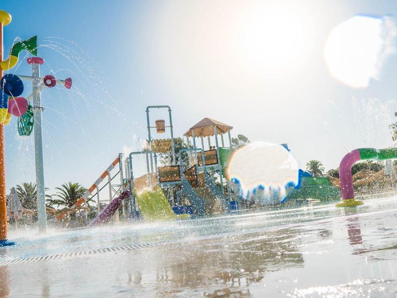 Bunter Wasserspielplatz mit Rutschen, Wasserfontänen und Sonnenschein an einem klaren Tag.