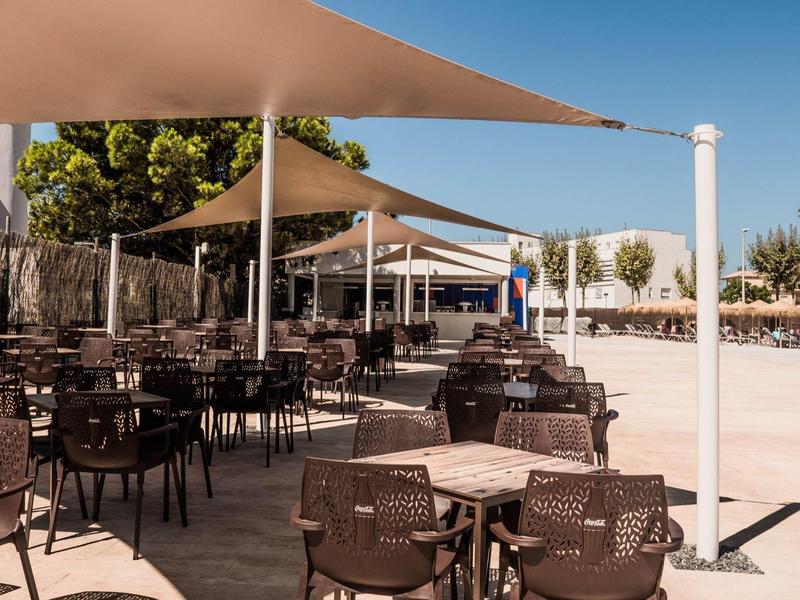 Leerer Außenbereich eines Cafés mit braunen Stühlen, Tischen und großen Sonnensegeln.