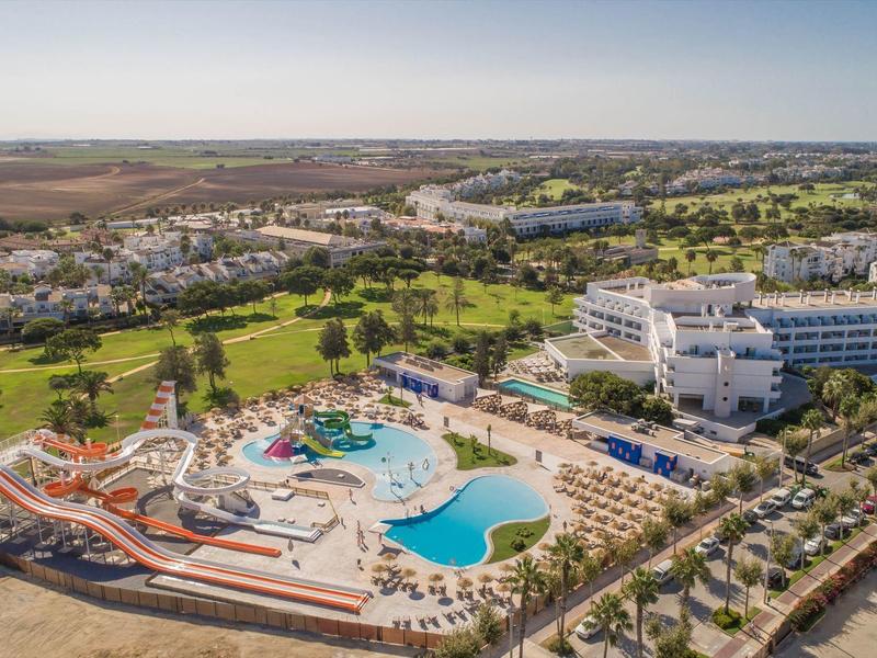 Große Hotelanlage mit Wasserpark, Pools, Palmen und grünen Golfplätzen in sonniger Landschaft.