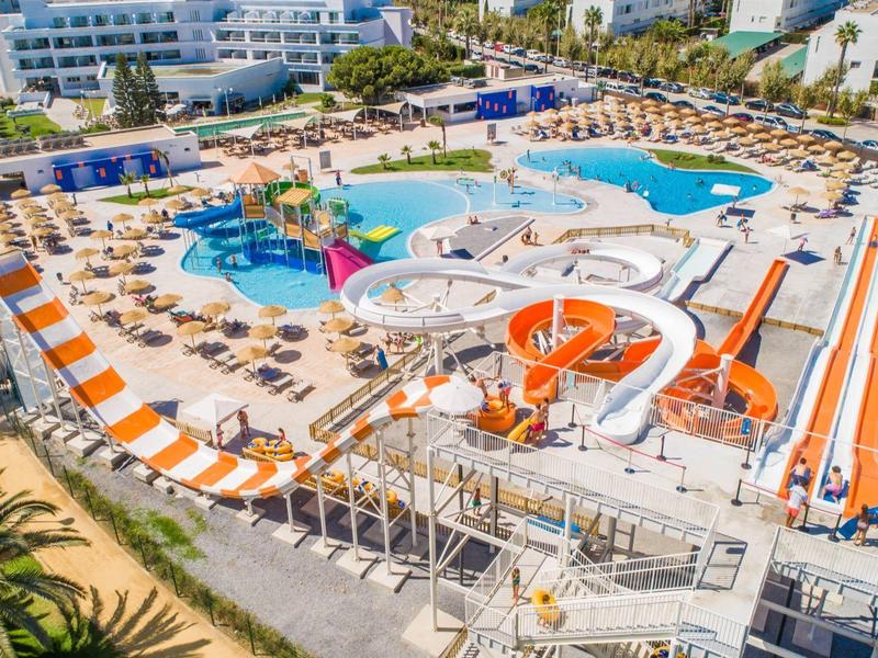 Großer Wasserpark mit Pools, bunten Wasserrutschen und Reihen von Liegestühlen mit orangefarbenen Sonnenschirmen.