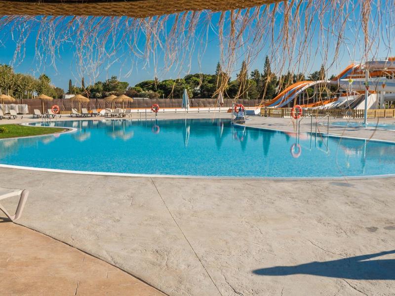 Großer, runder Pool mit blauer Wasserfläche umgeben von Liegestühlen und Sonnenschirmen.