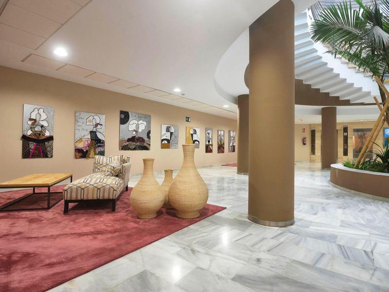 Moderner Innenraum mit Marmorfußboden, Säulen, Sitzbereich auf rotem Teppich und Pflanzenarrangement.