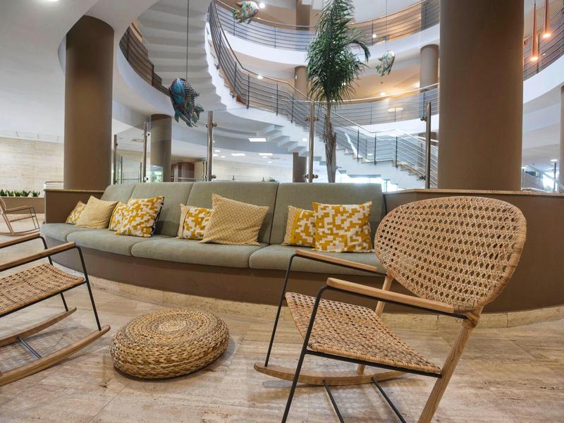 Moderne Lounge mit grauem Sofa, gelben Kissen, Korbsesseln und Holzboden in hellem Design.