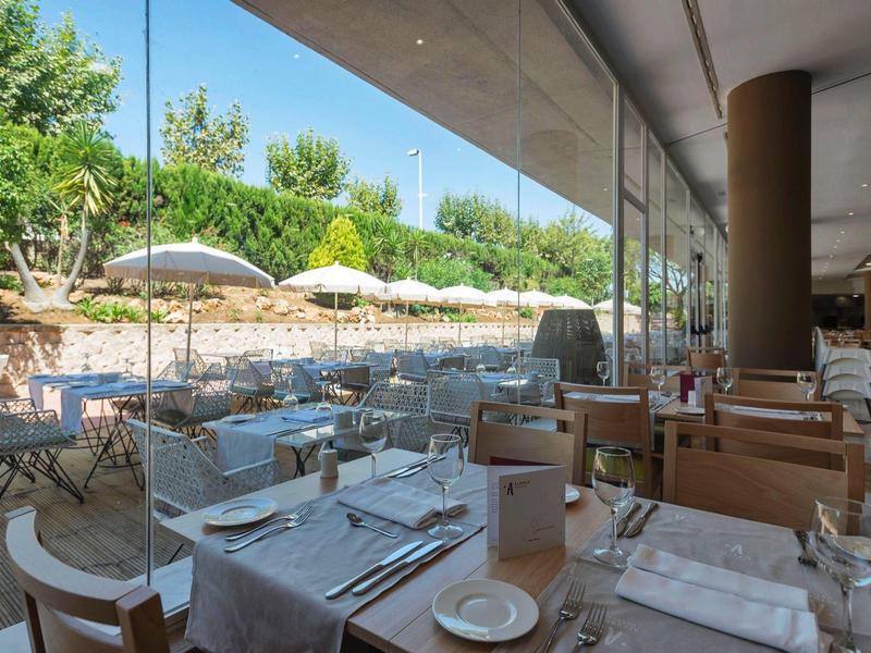 Modernes Restaurant mit großen Glasscheiben, gedeckten Tischen und Terrasse mit Sonnenschirmen.