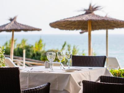 Tisch mit Gläsern auf Terrasse mit Blick aufs Meer und Strohmachschirme