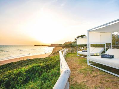 Moderne weiße Lounge-Betten mit Meerblick an einem Strand bei Sonnenuntergang.