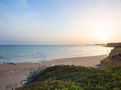 Strand mit ruhigem Meer, Sand und Klippen bei Sonnenuntergang