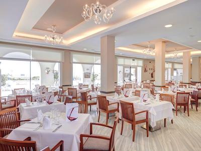 Hell eingerichteter Speisesaal mit gedeckten Tischen und Holzstühlen in einem Hotel.