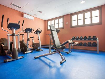 Fitnessraum mit blauen Boden, orangen Wänden, Trainingsgeräten und Hanteln an der Wand.