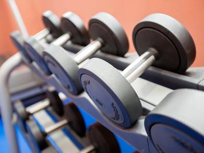 Nahaufnahme von Hanteln in einem Fitnessstudio mit orangener Wand im Hintergrund.