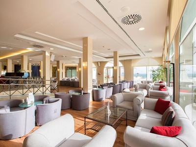 Helles Hotel-Loungesalon mit bequemen Sesseln und großen Fenstern mit Blick nach draußen.