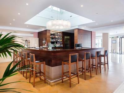 Moderner Hotelbar-Bereich mit Holzmöbeln und hellem Tageslicht durch großes Dachfenster.