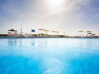 Blauer Pool mit klarem Wasser und Sonnenschirmen am Rand unter hellem Himmel.