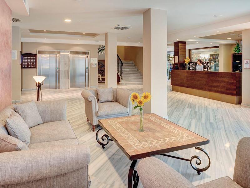 Heller, moderner Raum mit Sofa, Tisch, Sonnenblumen und Empfangstresen in warmen Farben.