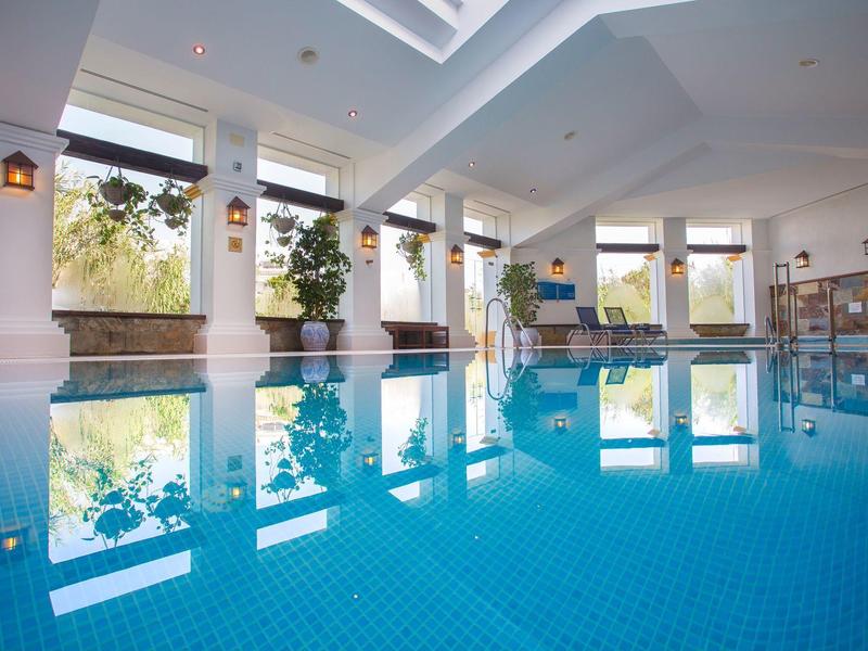 Hell beleuchtetes Hallenbad mit klarem blauem Wasser und großen Fenstern.