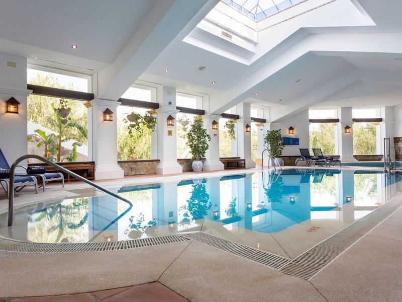 Innenpool mit Liegestühlen, großen Fenstern und Oberlicht, helle, moderne Gestaltung.