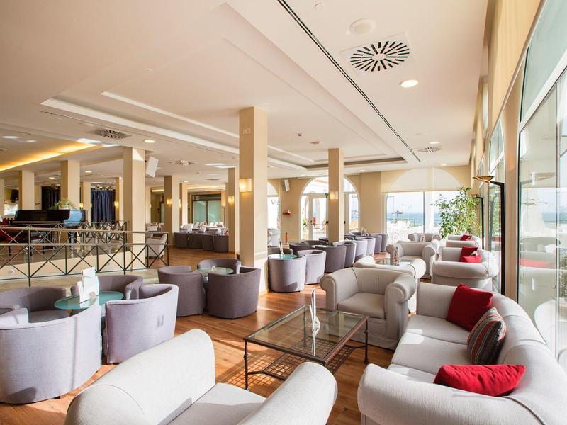 Helles, modernes Café mit großen Fenstern, bequemen Sesseln und Kissen in neutralen Farben.