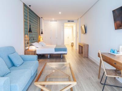 Habitación de hotel con mobiliario moderno, cama, sofá, escritorio y televisión.