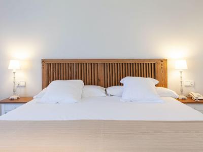 Una habitación de hotel sencilla con cama doble, cabecero de listones de madera y dos mesitas de noche con lámparas.
