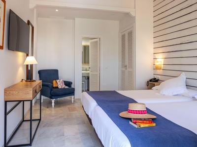Helles Hotelzimmer mit Doppelbett, blauem Sessel, weißer Wand und dekorativen Details.