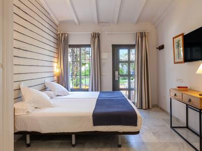 Helles Hotelzimmer mit Doppelbett, Fenster, Fernseher und modernem Mobiliar.