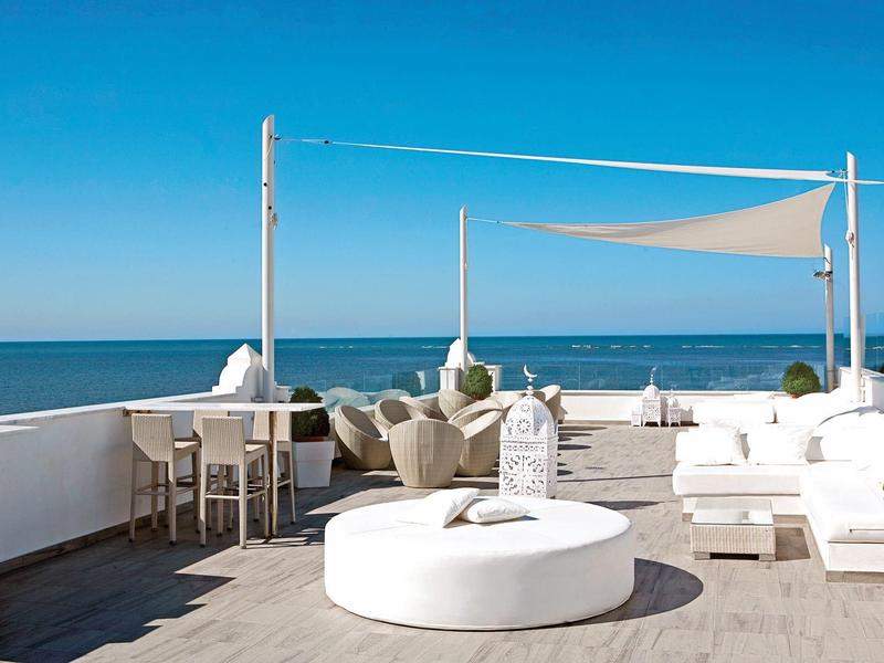 Terrazza moderna di un hotel con vista sul mare, arredi bianchi e tenda ombreggiante.