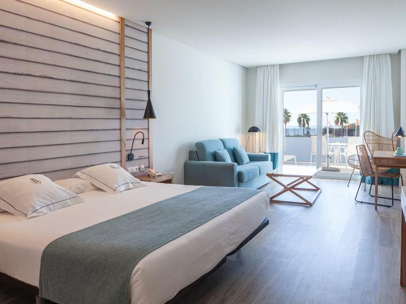 Camera d'hotel moderna con letto matrimoniale, divano blu, scrivania e balcone luminoso.