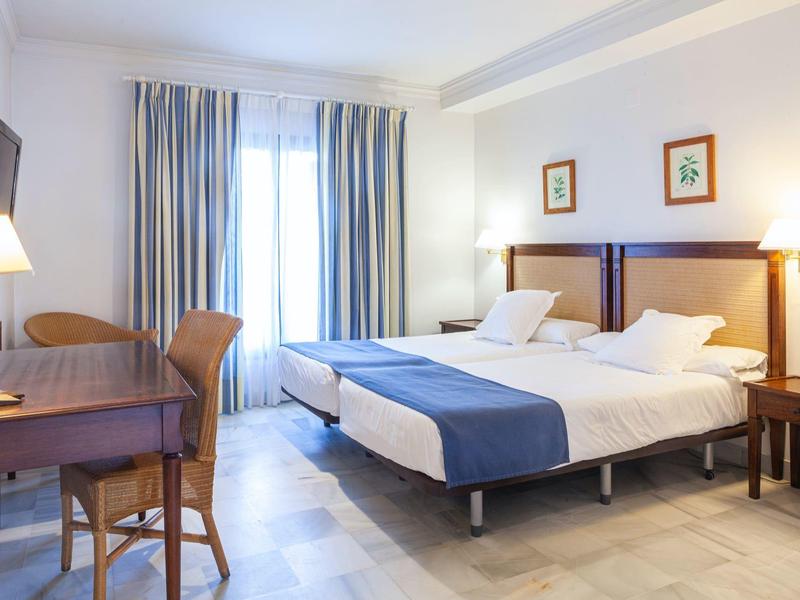 Camera d'hotel luminosa con letto matrimoniale, scrivania, sedie e finestra con tende.