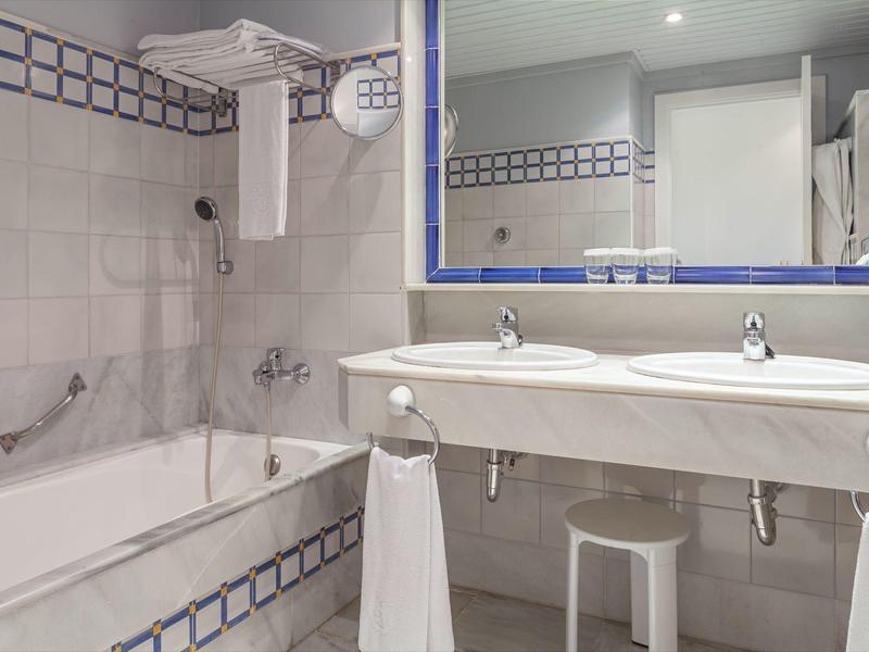 Bagno d'hotel con vasca da bagno, doppi lavandini e grande specchio incorniciato di blu.