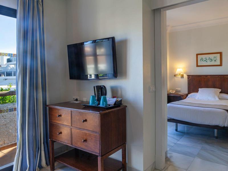 Camera d'hotel con letto matrimoniale, TV a parete e balcone con vista sul giardino.