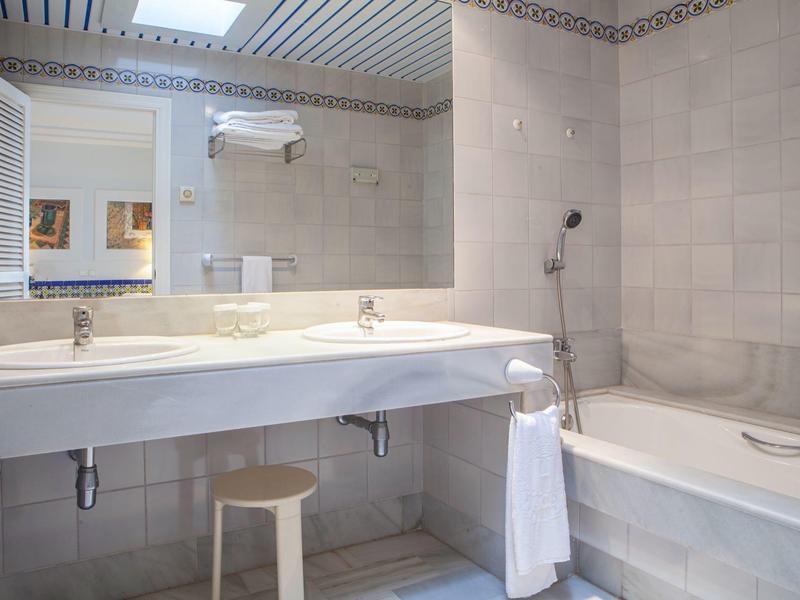 Bagno d'hotel moderno con doppi lavandini, sgabello, vasca da bagno e grande specchio.