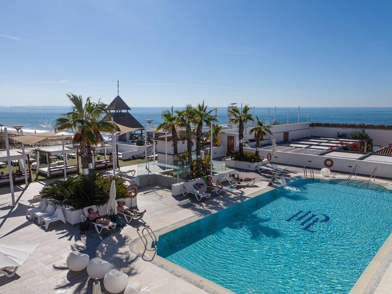 Piscina all'aperto con palme e vista sul mare sotto un cielo limpido.