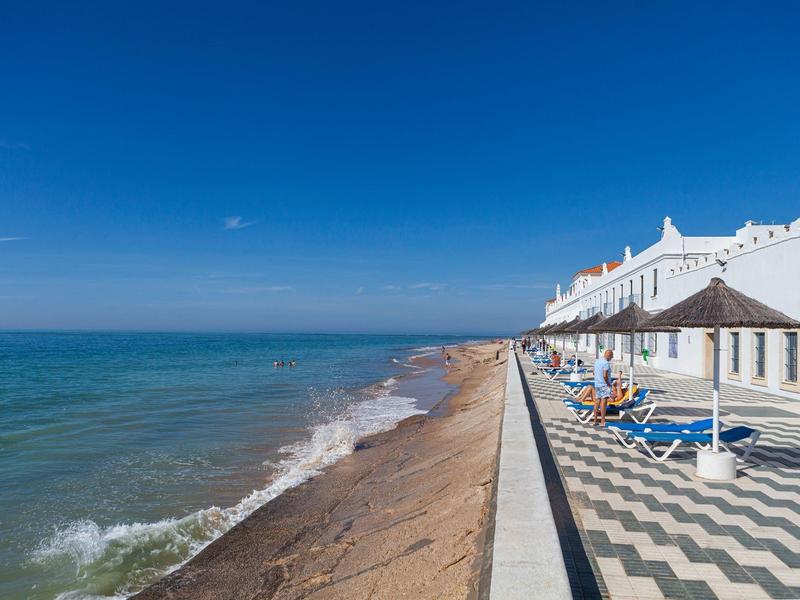 Spiaggia con passeggiata, mare calmo e lettini sotto un cielo azzurro.
