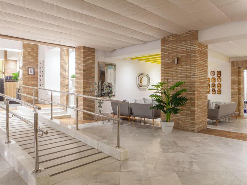 Atrio ampio e luminoso con poltrone, piante e corrimano per accesso.