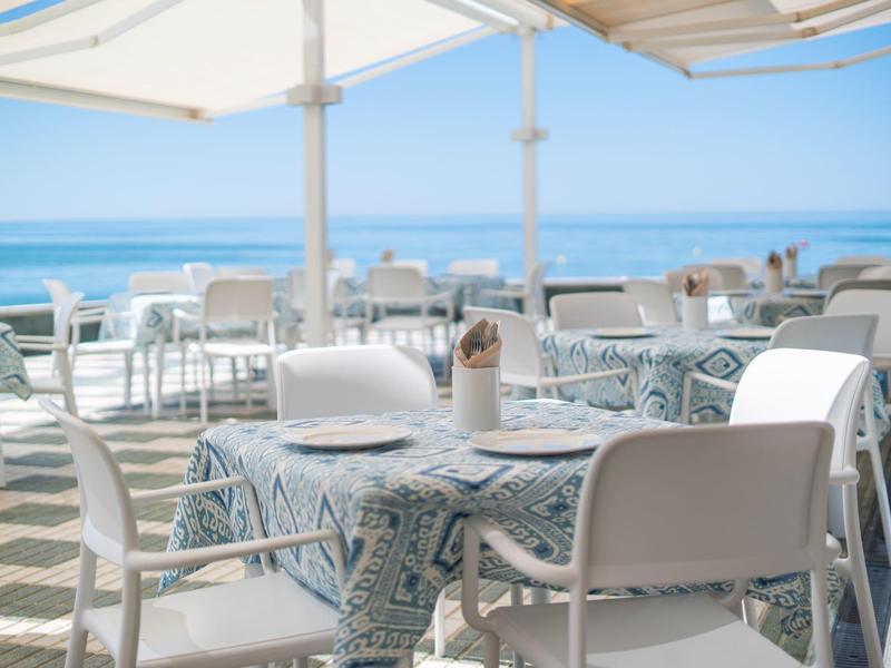 Terrazza di ristorante sul mare con tavoli coperti da tovaglie blu.