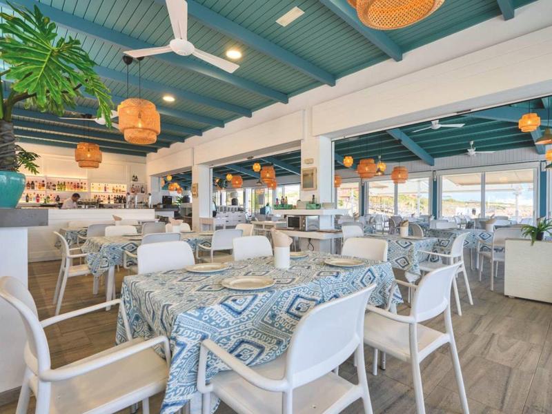 Ristorante luminoso con tavoli decorati e sedie bianche, ambiente accogliente e moderno.