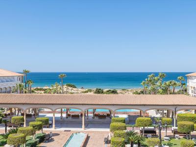 Vista sul mare da una terrazza dell'hotel con giardino, piscina e palme sotto un cielo azzurro.