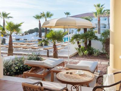 Blick von einer Terrasse mit Stühlen und Tisch auf Pool, Sonnenliegen und Palmen im Hotel.