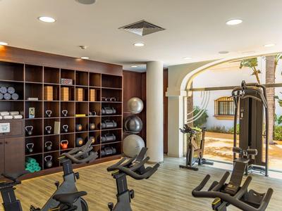 Moderner Fitnessraum mit Trainingsgeräten und Blick auf einen Außenbereich mit Pflanzen.