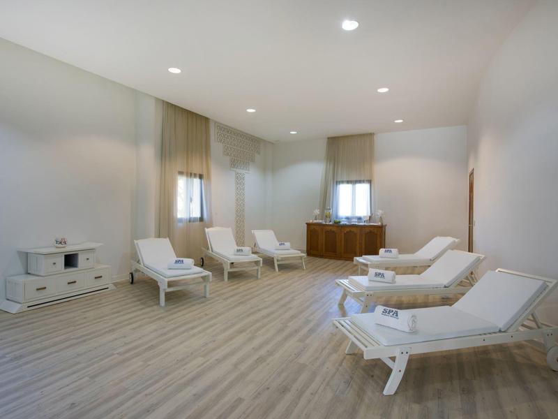 Lichte ontspanningsruimte met witte ligstoelen, houten vloer en zachte verlichting.