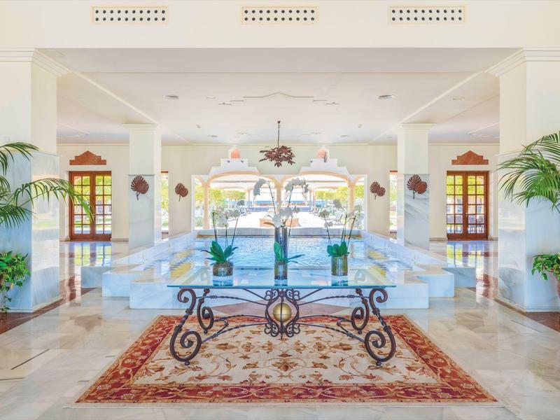 Lichte hotellobby met witte bank, glazen tafel en exotische planten.