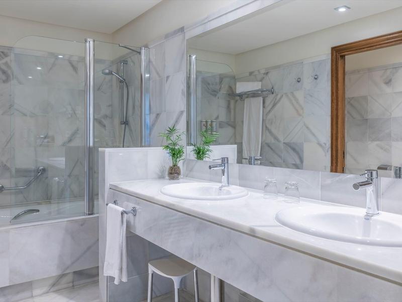 Moderne badkamer met dubbele wastafel, spiegel en badkuip met glazen afscheiding.