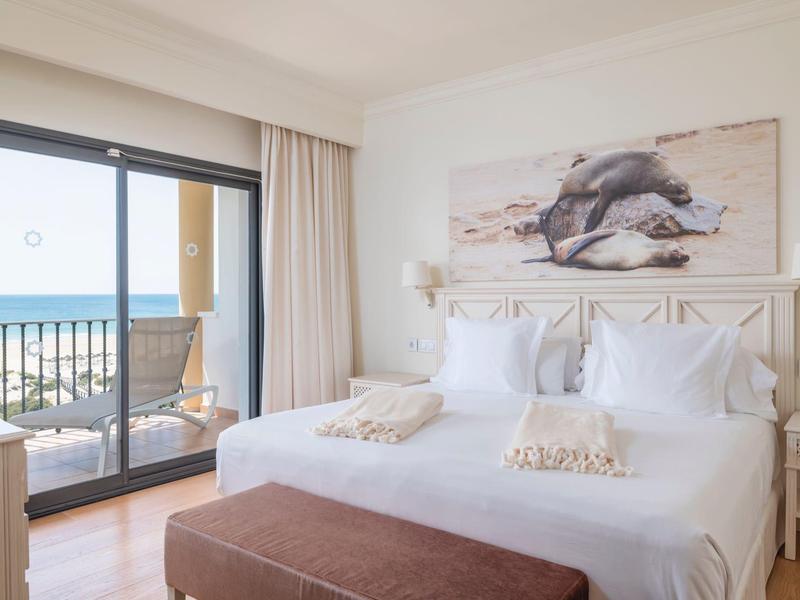 Lichte slaapkamer met twee eenpersoonsbedden, kunst boven het hoofdeinde en een balkon met zeezicht.