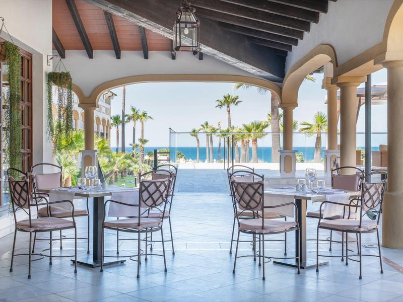 Overdekt terras met tafels en stoelen met uitzicht op het zwembad en de zee.
